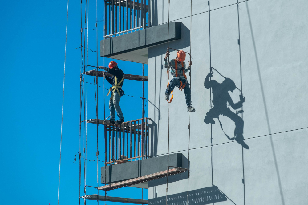 Trabalhadores em altura utilizando equipamentos de segurança durante serviço na fachada de um edifício.